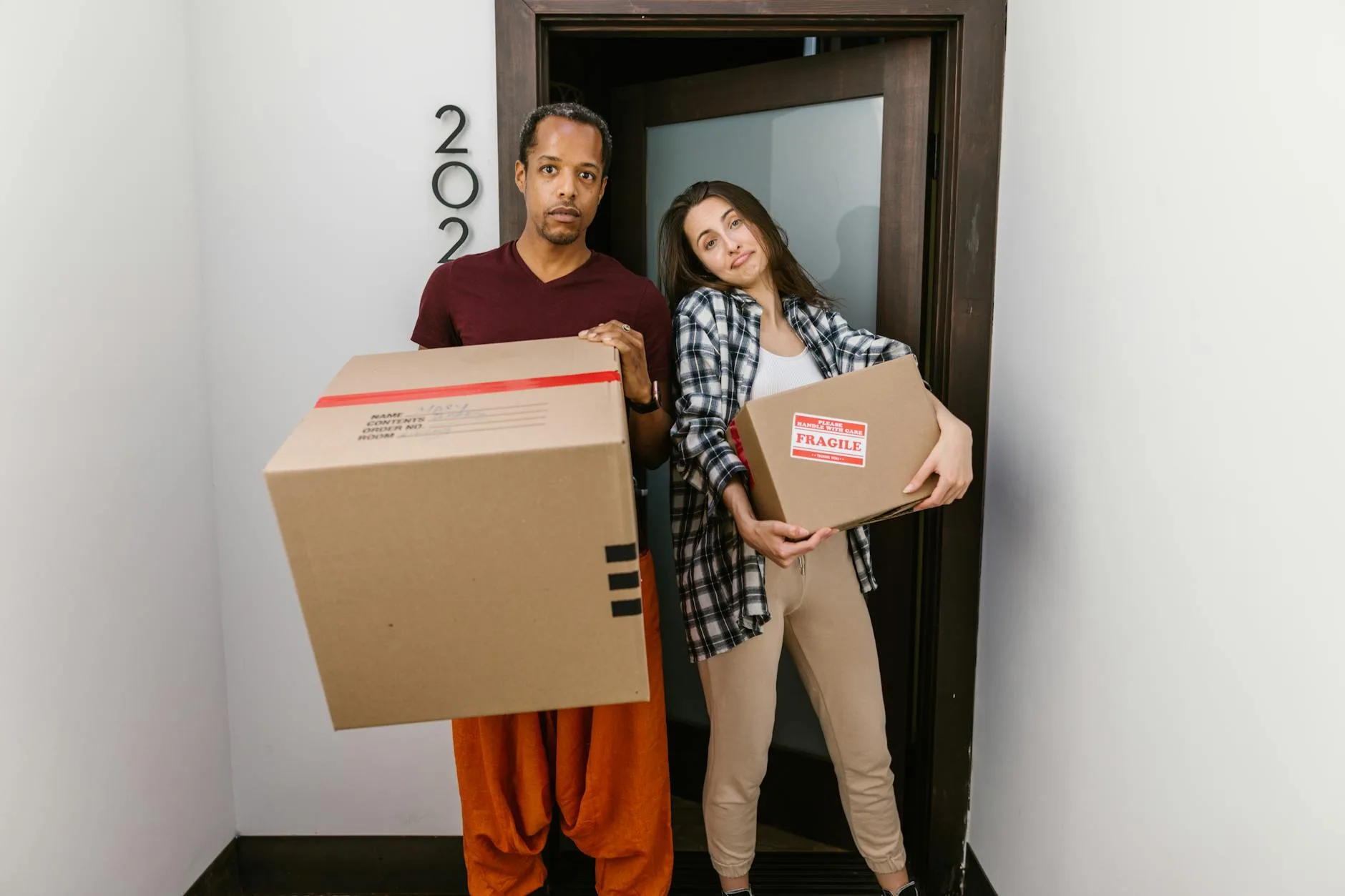 Couple portant des cartons de déménagement étiquetés « fragile » dans l'entrée d'un immeuble